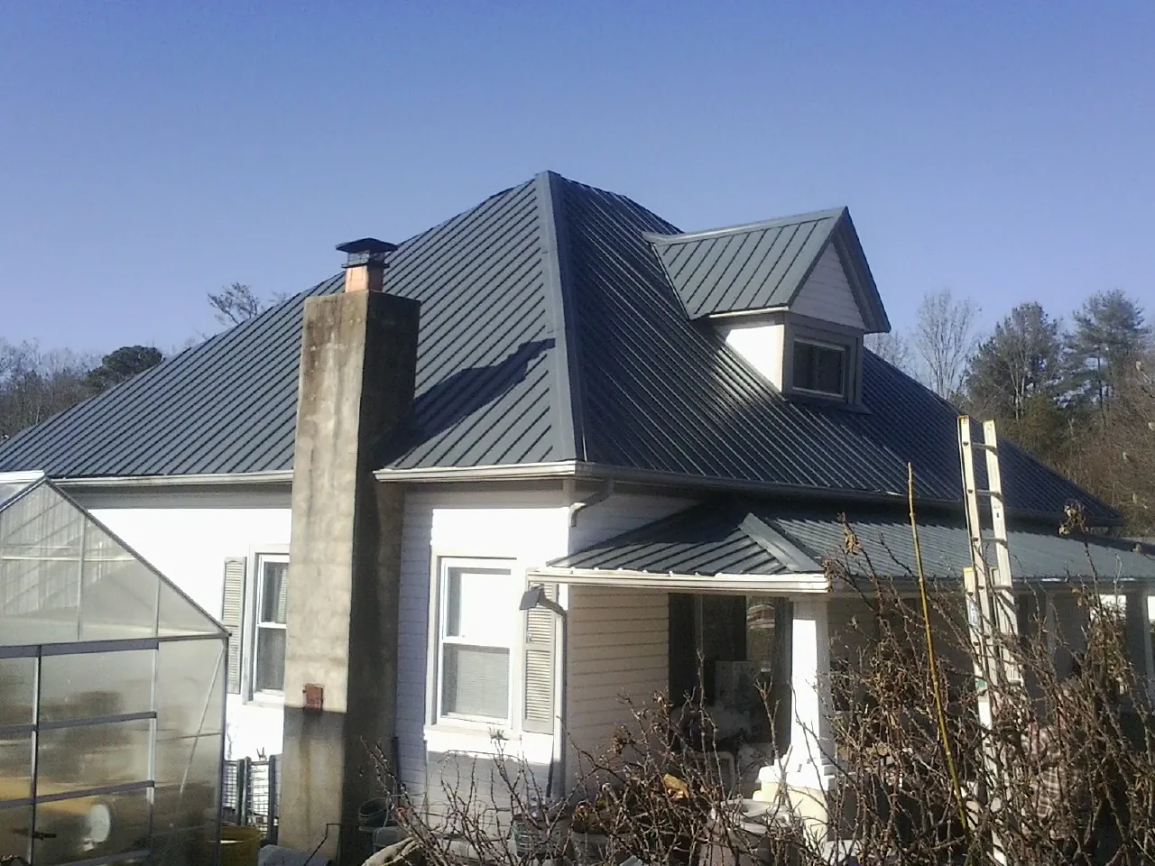 Dark blue standing seam metal roof on a white farmhouse with dormer — Slate & Tile Roof Repair by Roofing Brothers in West Farmington