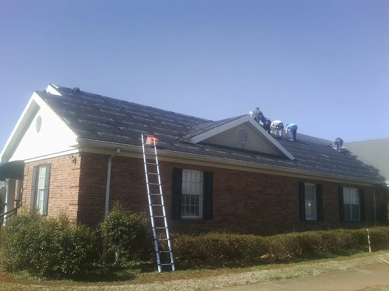 Crew tearing shingles off a brick ranch roof with a ladder set — Metal Roof Repair work by our crew in West Farmington