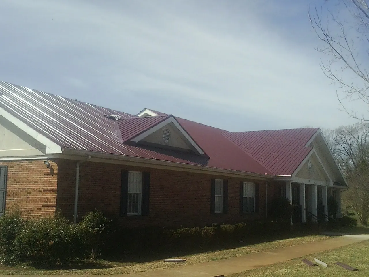 Red metal roof with gabled entries on a long brick building, from a Hail Damage Roof Repair job in West Farmington