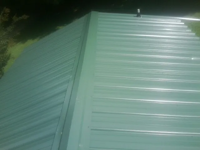 New green metal panels meeting at the ridge of a roof — Flat Roof Repair work by our crew in West Farmington