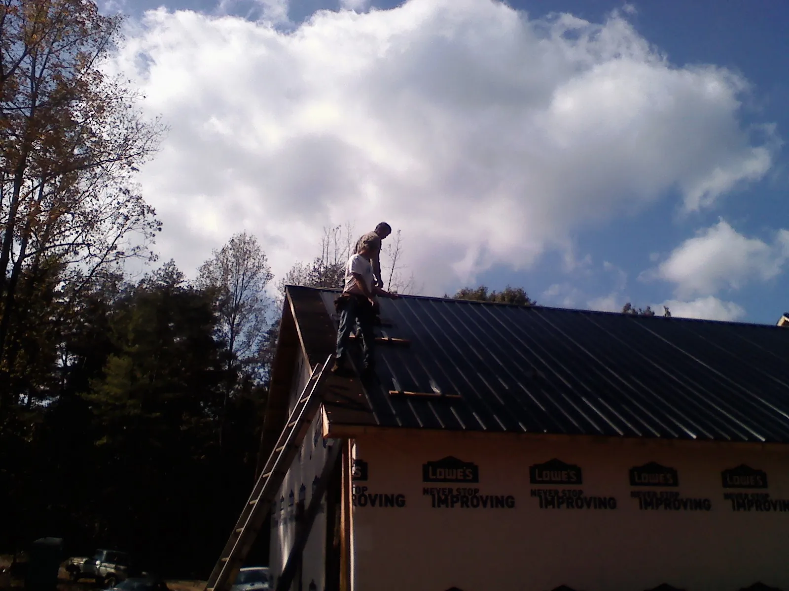 Roofer fastening dark metal panels high against a cloudy sky, from a Roof Inspection job in West Farmington