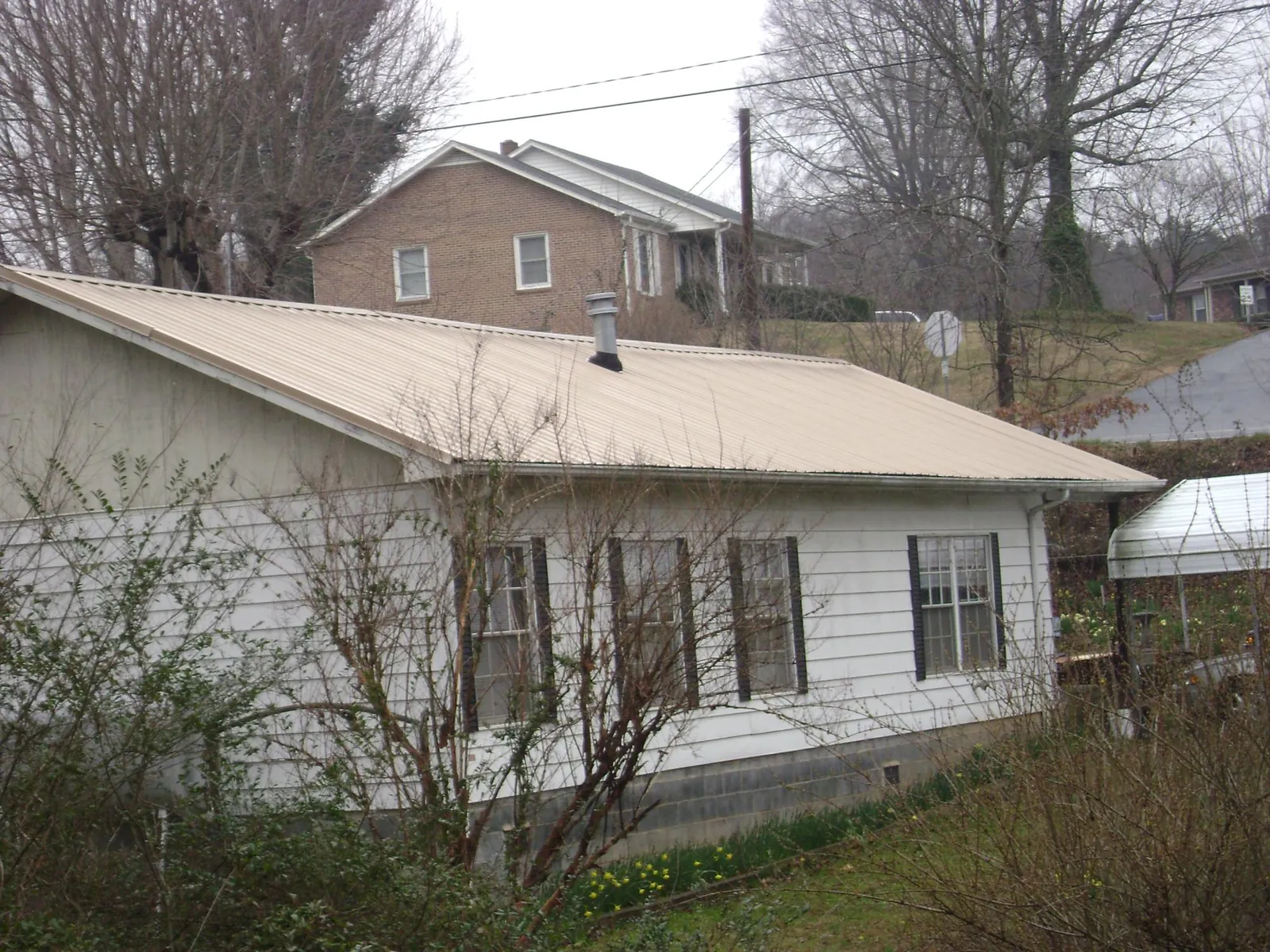 Tan metal roof on a white sided house set into a hillside — Commercial Roofing by Roofing Brothers in West Farmington