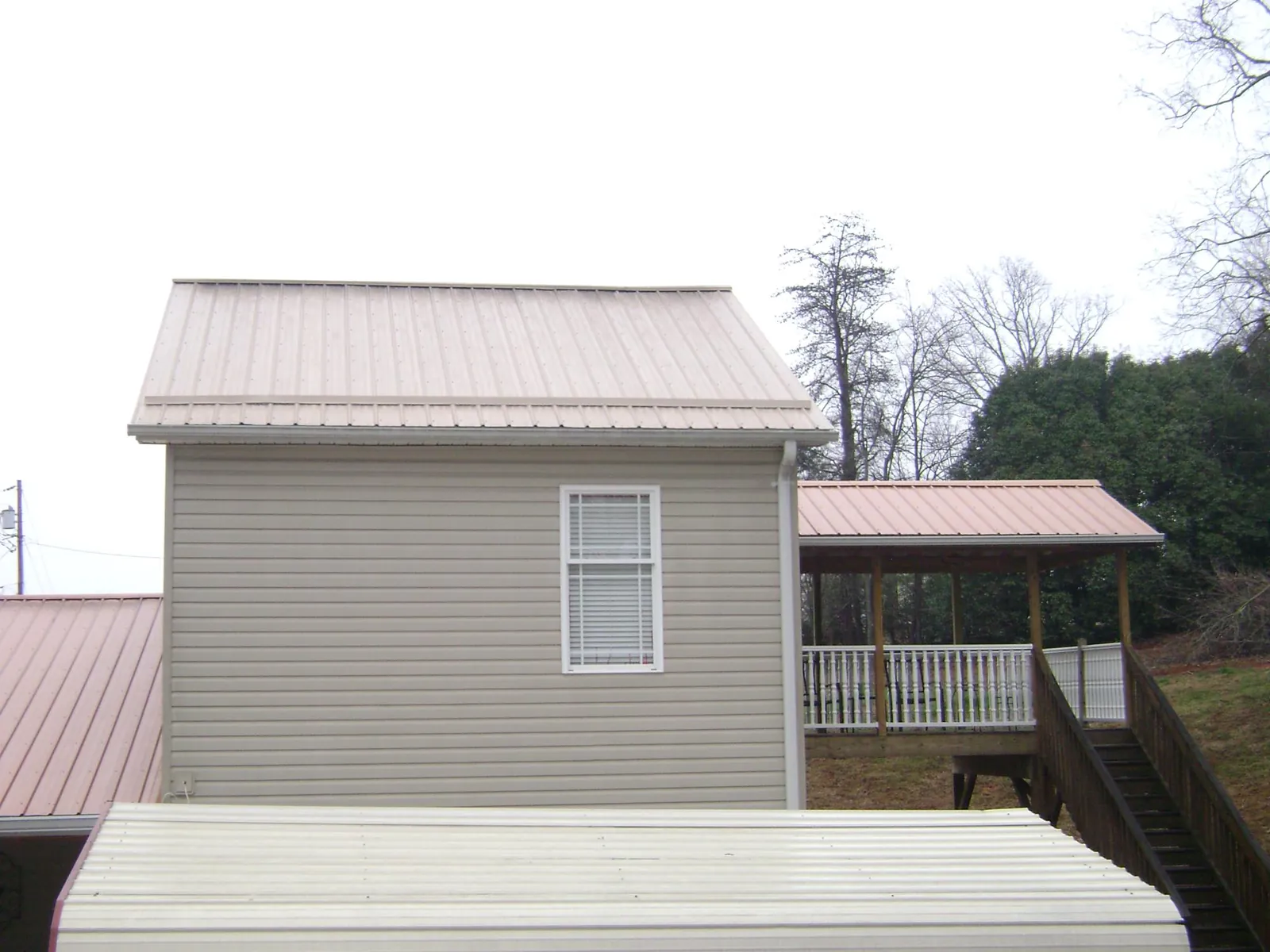 Tan metal roofs on a two story addition and attached porch, from a Roof Replacement job in West Farmington